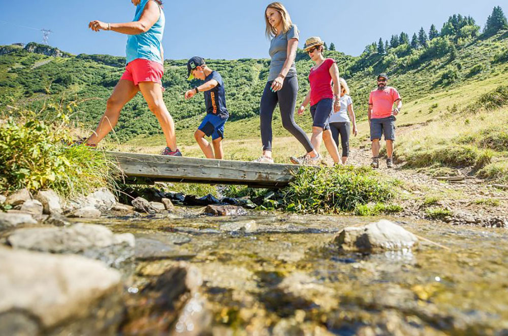famille en pleine randonnée en montagne en été passant sur un pont