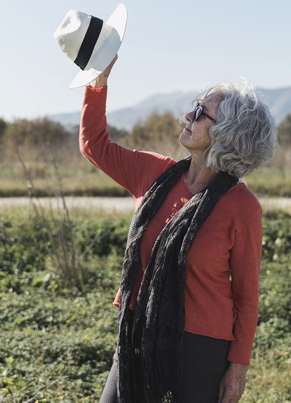 Femme agée aux cheveux blancs mettant un chapeau en face d'elle pour se proteger du soleil